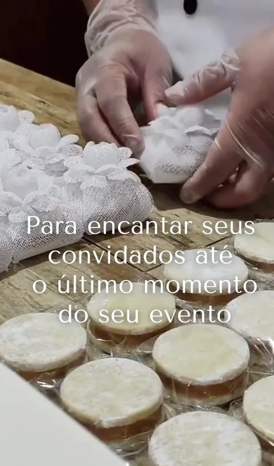 Alfajores sendo embalados à mão em tecido de renda branca para eventos